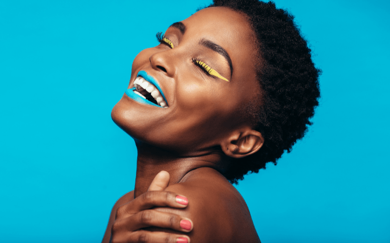 portrait of happy model with bright lipstick and eyeliner, in front of bright blue background