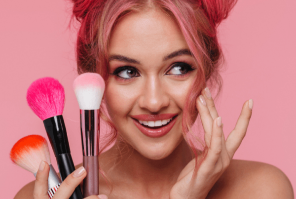 Portrait of beautiful shirtless woman with colorful hairstyle holding makeup brushes isolated over pink background