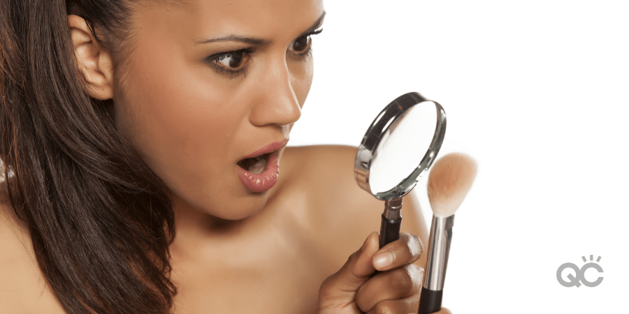 woman shocked as she looks at makeup brush through magnifying glass