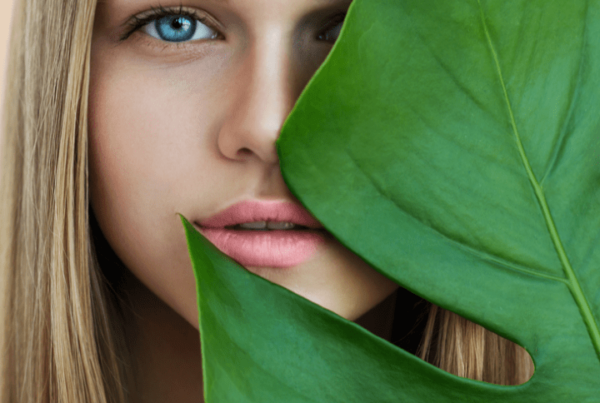 Beauty smiling blonde model with natural make up and green leaves. Copy space. Spa and wellness. Close up, selective focus.