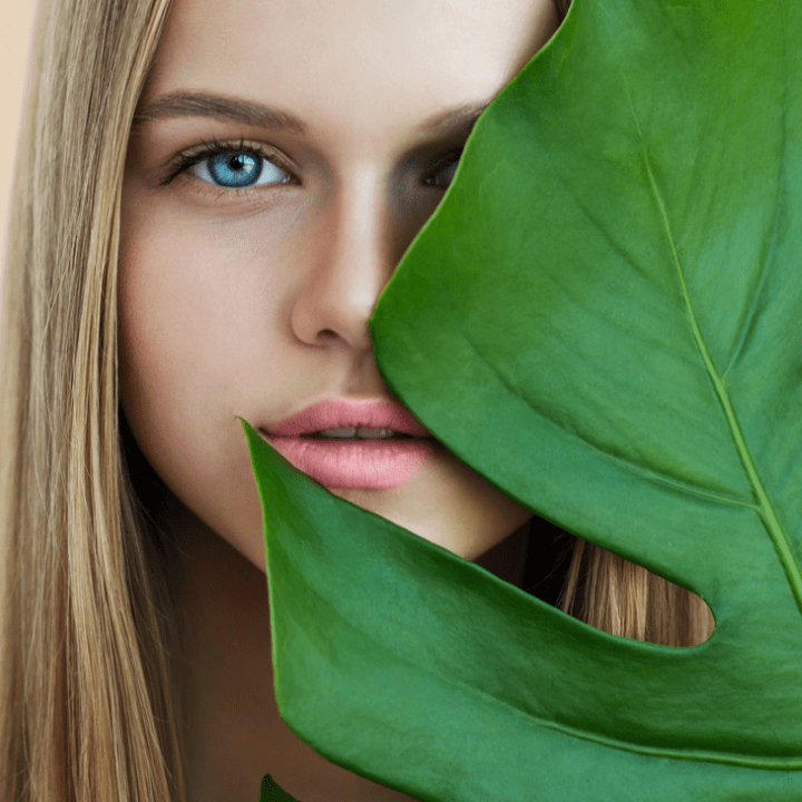 Beauty smiling blonde model with natural make up and green leaves. Copy space. Spa and wellness. Close up, selective focus.