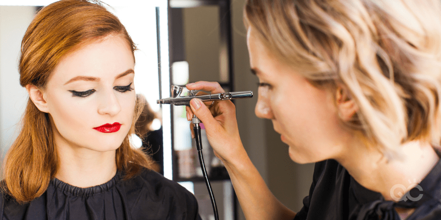 mua applying makeup on client using airbrush machine