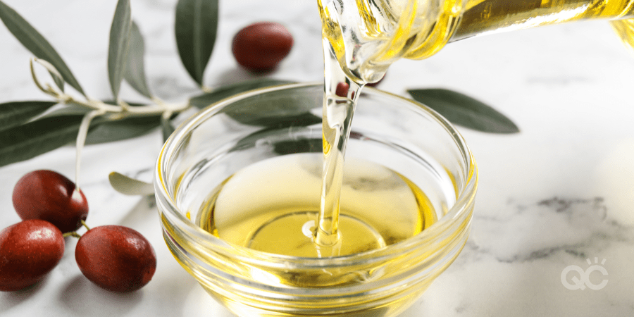 Pouring with jojoba oil from jug into bowl on white marble table