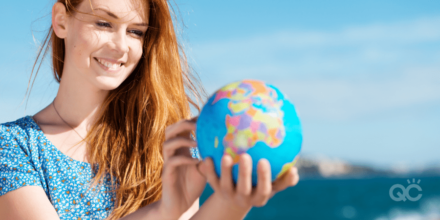 Smiling beautiful young woman standing in the summer sunshine holding a globe at the sea with copyspace