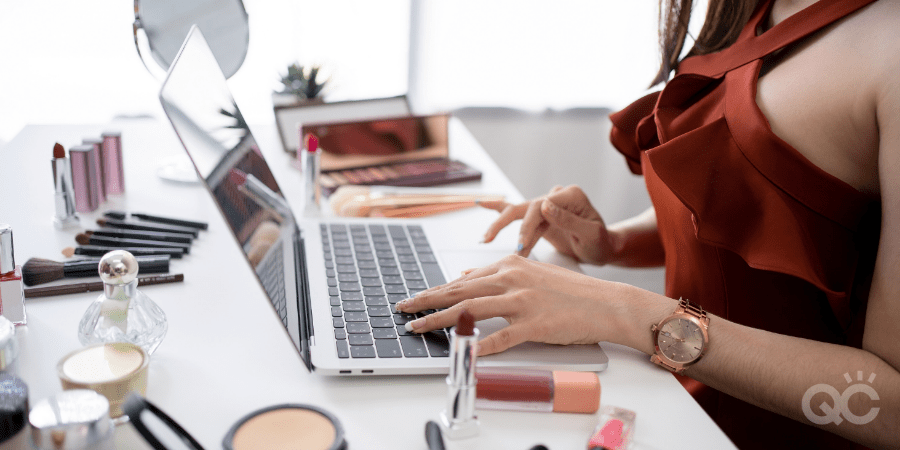 makeup artist on laptop, surrounding by makeup products on table