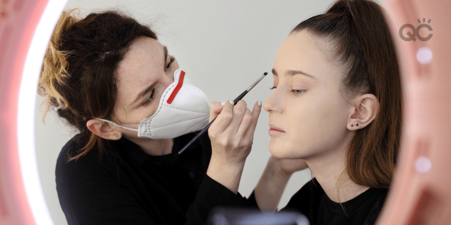 makeup artist wearing face mask and applying makeup to female client