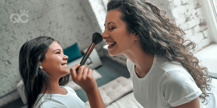 mother becoming a makeup artist at home, daughter brushing nose with makeup brush