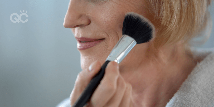 older woman applying powder to face using powder brush