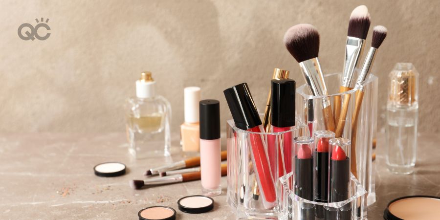 Lipstick holder with different makeup products on table against color background.