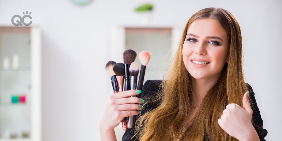 Happy woman holding up makeup brushes and giving thumbs up