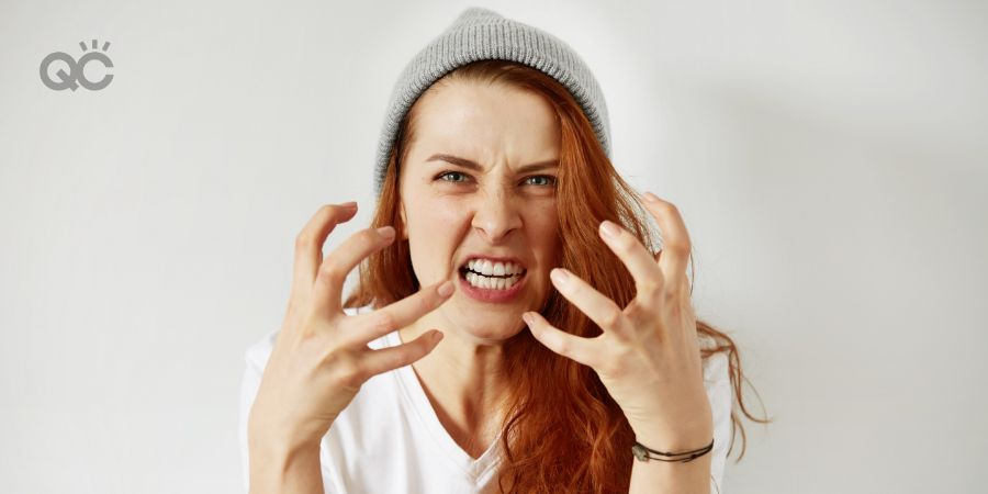 Close up isolated portrait of young annoyed angry woman holding hands in furious gesture. Young female with red hair in white T-shirt and cap. Negative human emotions, face expressions.