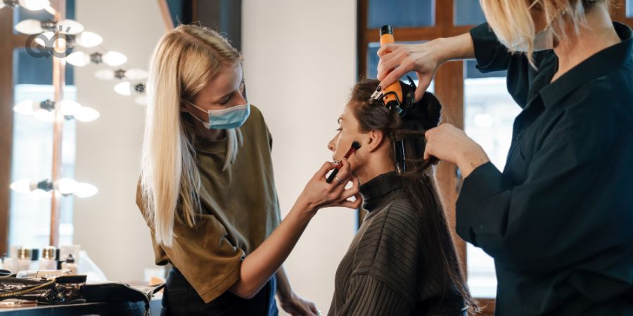 Makeup artist and hair stylist working on client at the same time in salon