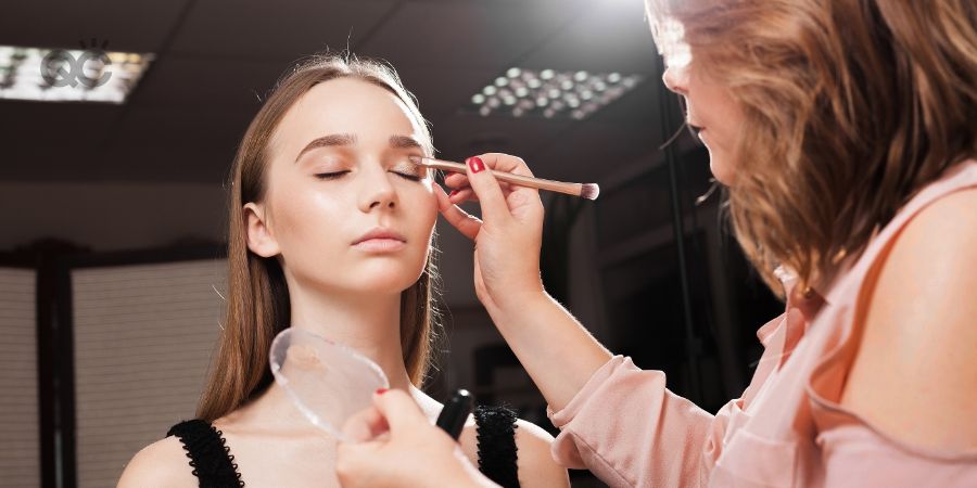 makeup artist appling a primer on an eyelid of a young beautiful woman using a brush before dabbing eyeshadows. concept of professional make up training