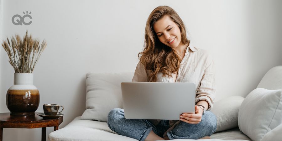 Portrait of a young female freelancer sitting on the couch and using laptop at home happily.