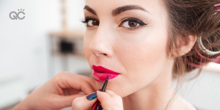 Makeup artist applying bright pink lipstick to lips of young woman in curlers