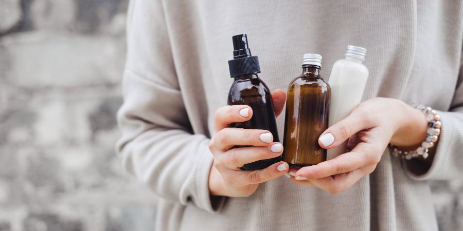 Woman's holding botles with spa cosmetics against gray wall. Beauty blogger, salon therapy, minimalism concept, copyspace. Skincare labels article.