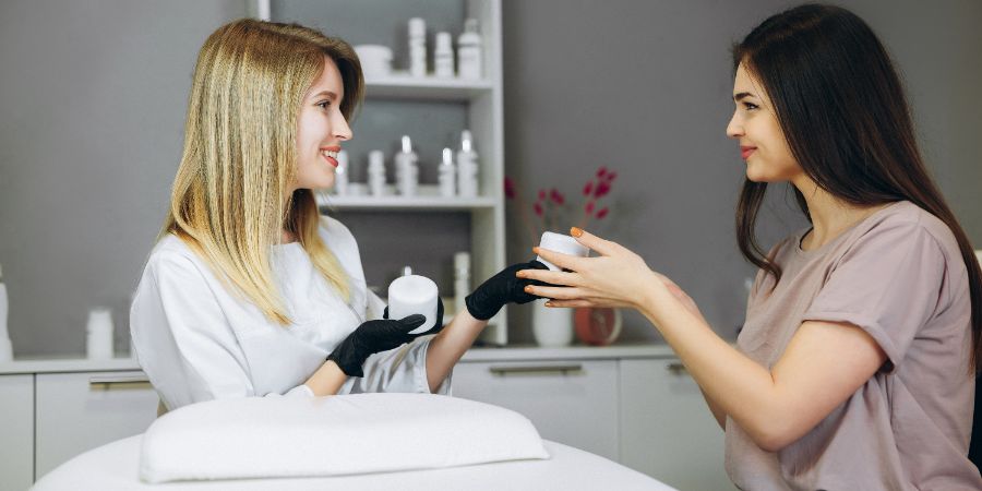 Consultation in cosmetology clinic. Female beauty doctor talking with patient and selling cream or mask. Skincare consultant article.