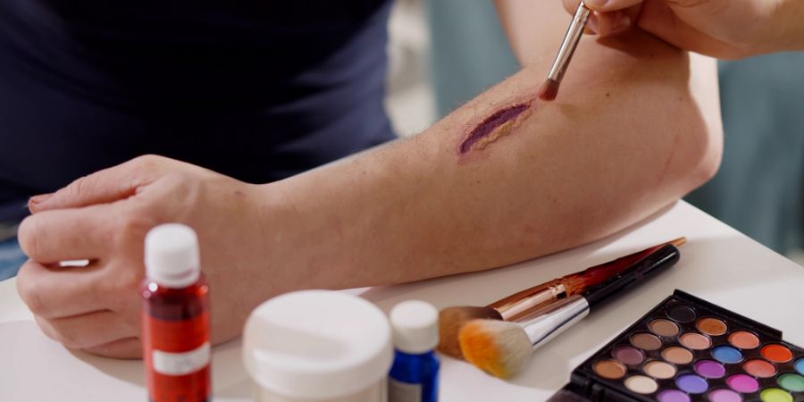 Special effects makeup artist applying fake wound to client's arm.