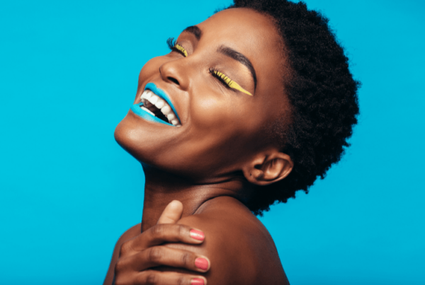 portrait of happy model with bright lipstick and eyeliner, in front of bright blue background