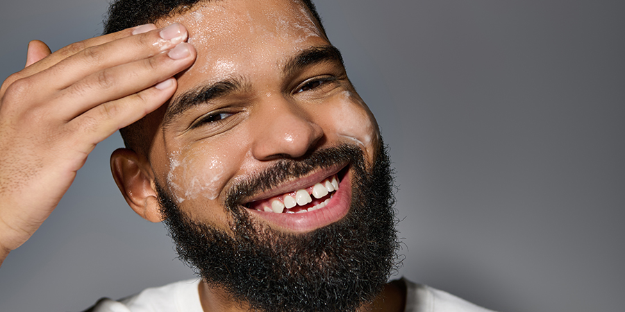 Happy man benefitting from a strong skincare routine and applying facewash to face