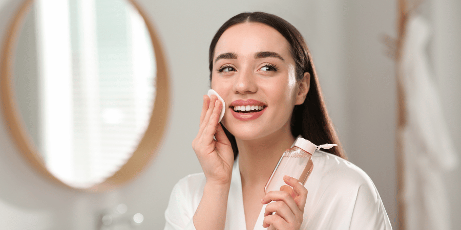 Woman in white robe removes makeup using makeup remover